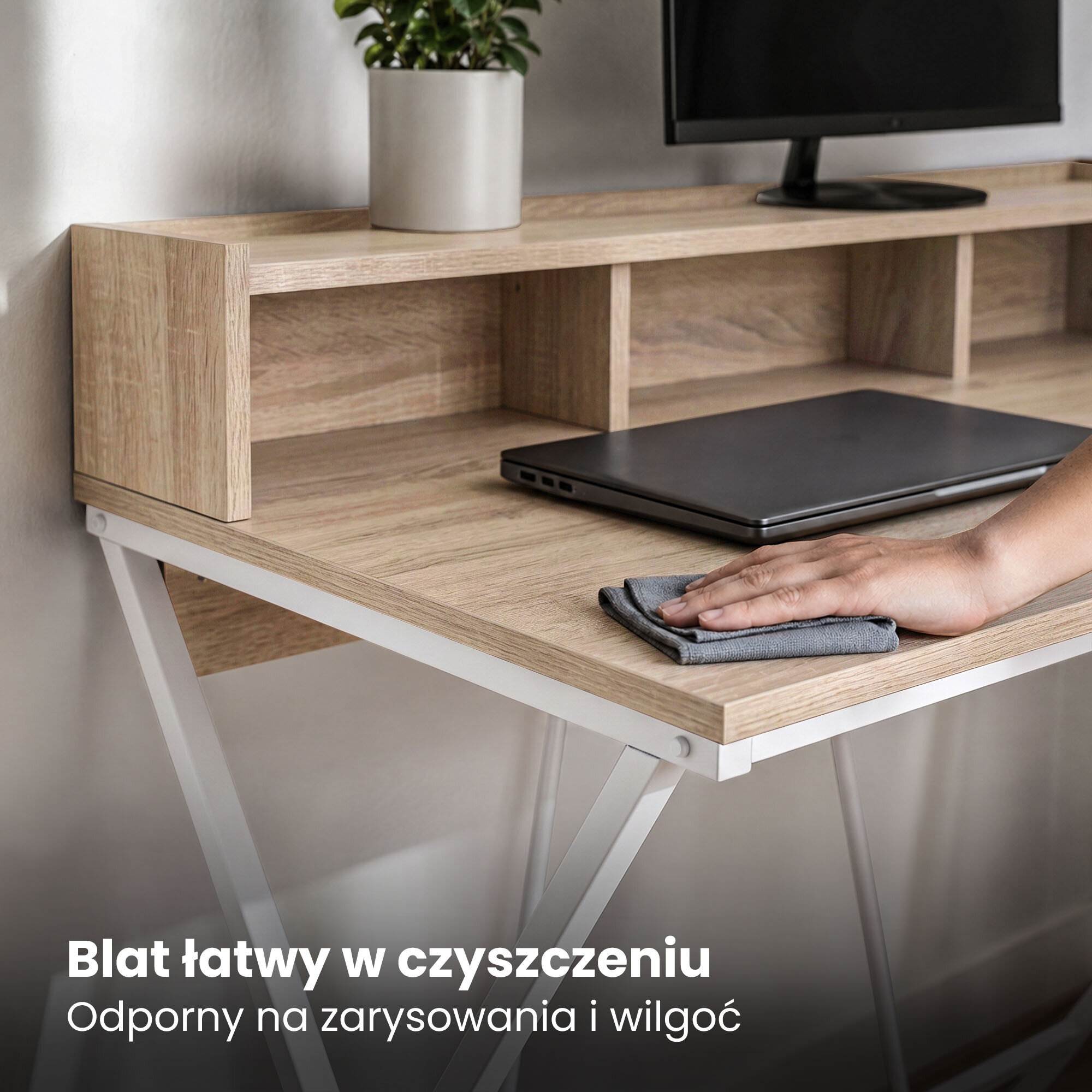 Biurko z blatem w kolorze dębu Sonoma, z białymi nogami, na którym znajduje się laptop i ręka czyszcząca powierzchnię. Tekst na obrazie: \'Blat łatwy w czyszczeniu, Odporny na zarysowania i wilgoć\'.