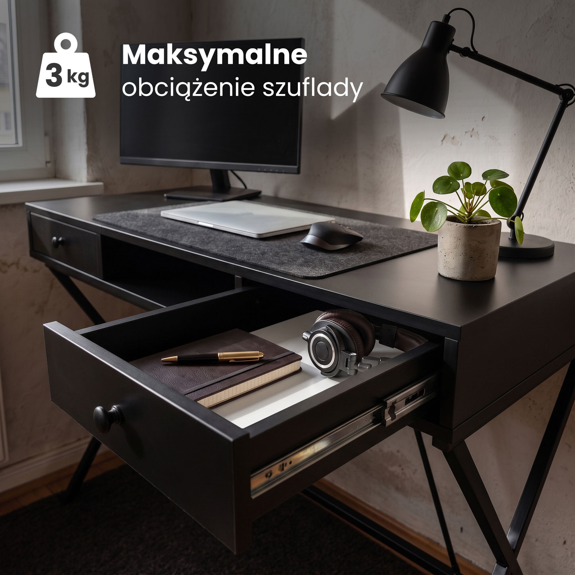 Czarne biurko z otwartą szufladą, w której znajdują się notes, długopis i słuchawki. Na biurku stoi monitor, laptop, myszka, lampa i roślina w doniczce; tekst na obrazie: \'Maksymalne obciążenie szuflady 3 kg\'.
