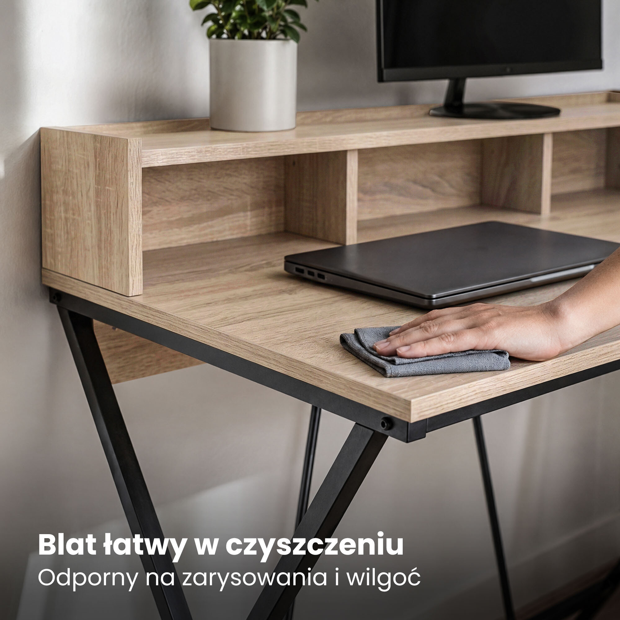 Biurko z blatem w kolorze dębu Sonoma, czarne nogi, na blacie laptop i ręka czyszcząca powierzchnię. Tekst na obrazie: \'Blat łatwy w czyszczeniu Odporny na zarysowania i wilgoć\'.