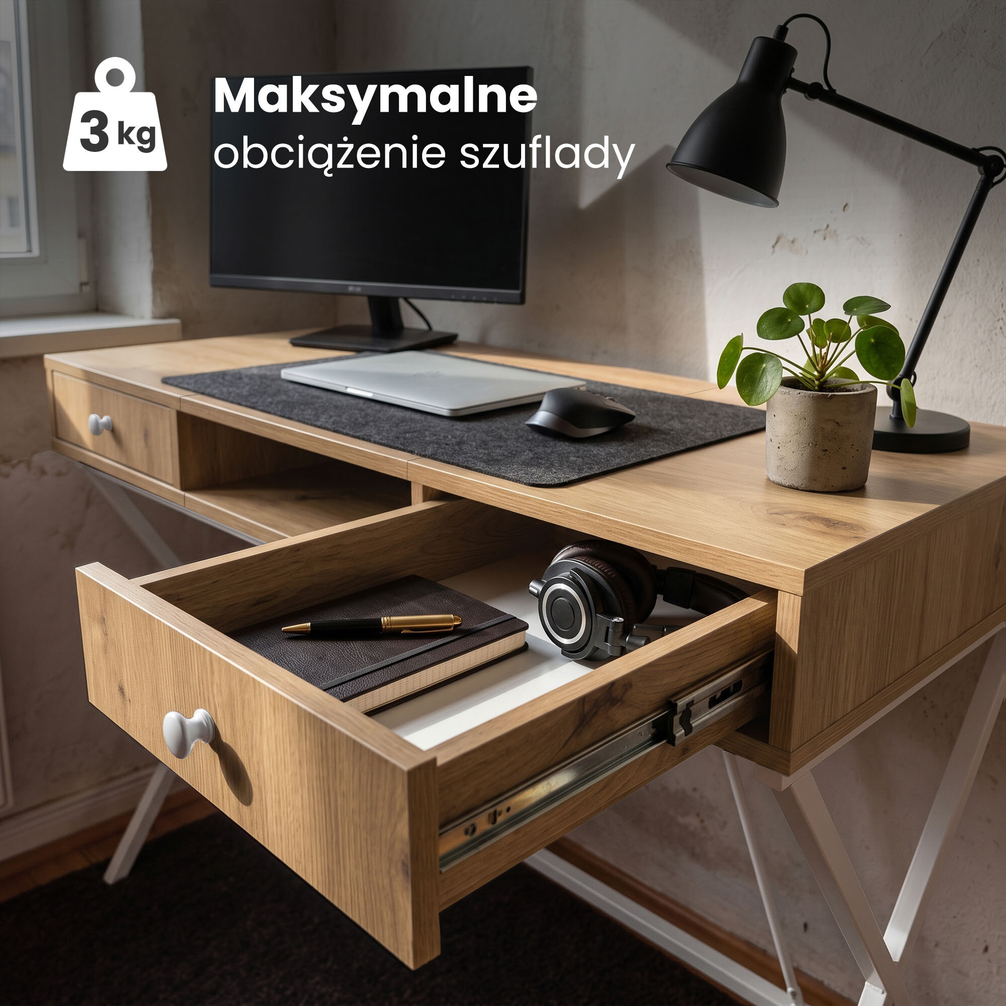 Biurko z drewnianym blatem i białymi nogami, na którym znajduje się monitor, laptop, myszka, lampa i roślina w doniczce. Otwarta szuflada zawiera notes, długopis i słuchawki, a na obrazie widoczny jest tekst: \'Maksymalne obciążenie szuflady 3 kg\'.