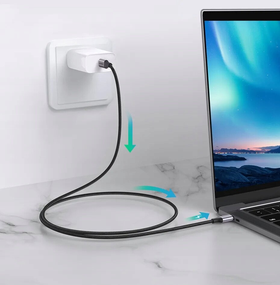 Na obrazie widać kabel USB-C podłączony do laptopa i ładowarki w gniazdku ściennym. Kabel leży na marmurowej powierzchni, a na ekranie laptopa widoczny jest krajobraz z zorzą polarną.