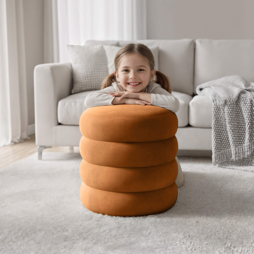 Na obrazie znajduje się pufa otwierana ze schowkiem w kolorze miedzianym, wykonana z weluru. W tle widoczna jest jasna sofa z poduszką i kocem.