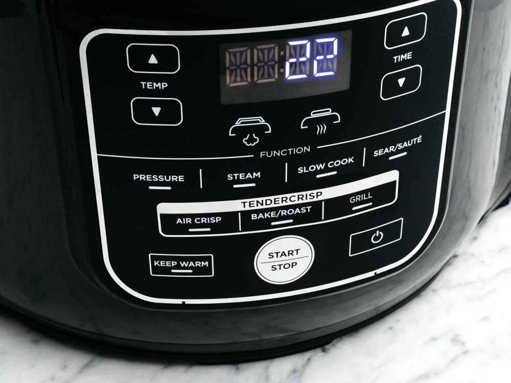Panel sterowania urządzenia kuchennego z wyświetlaczem cyfrowym pokazującym \'00:20\' oraz przyciskami do regulacji temperatury, czasu i funkcji takich jak \'Pressure\', \'Steam\', \'Slow Cook\', \'Sear/Sauté\', \'Air Crisp\', \'Bake/Roast\', \'Grill\'.