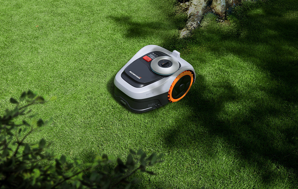 Robot koszący na trawie, z widocznym logo \'SEGWAY\' na górnej części obudowy. Urządzenie ma szary kolor z pomarańczowymi akcentami na kołach.