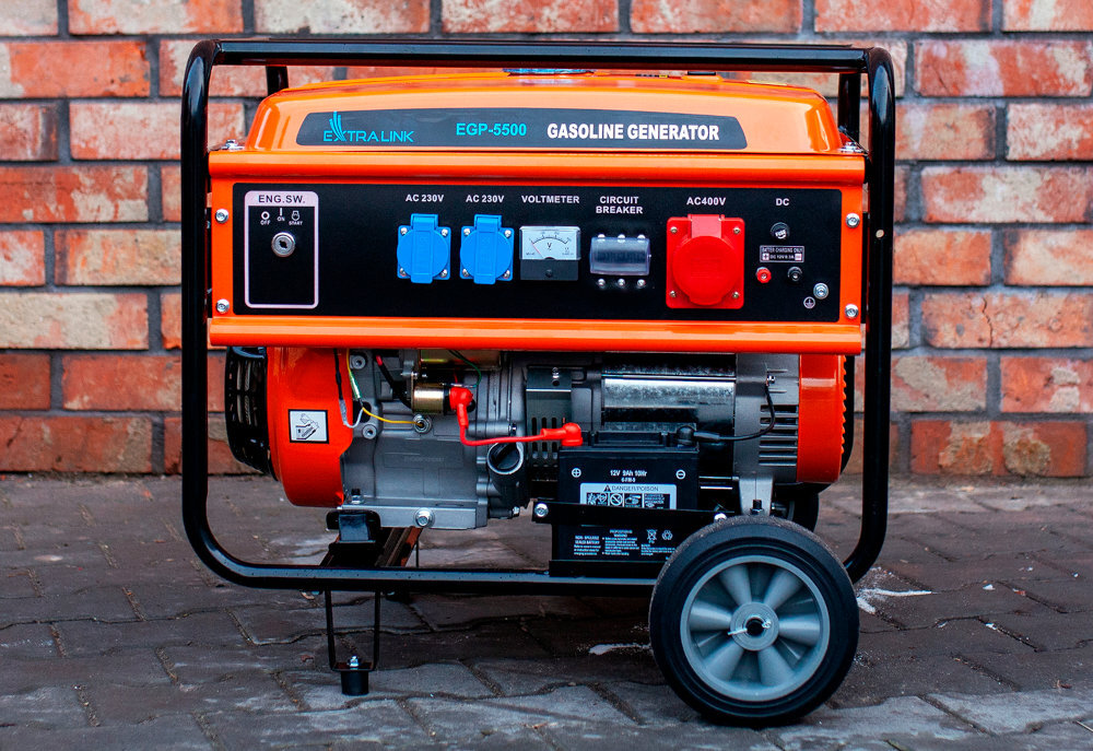 Na tle ceglanej ściany znajduje się pomarańczowy agregat prądotwórczy z widocznymi gniazdami i miernikiem. Na obudowie widnieje napis \'EXTRALINK EGP-5500 GASOLINE GENERATOR\'.