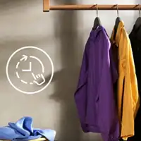 Na obrazie widoczne są trzy ubrania wiszące na wieszakach oraz symbol zegara z ręką wskazującą na tarczę. Ubrania mają kolory fioletowy, żółty i czarny.