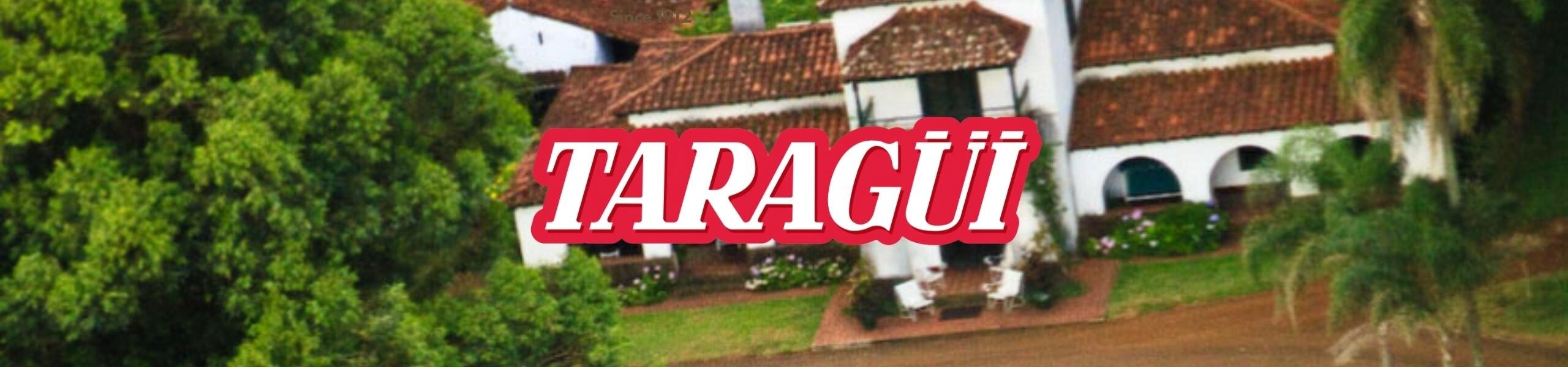 Na obrazie widoczny jest napis \'TARAGÜI\' na tle budynku z czerwonym dachem i otoczeniem zieleni.