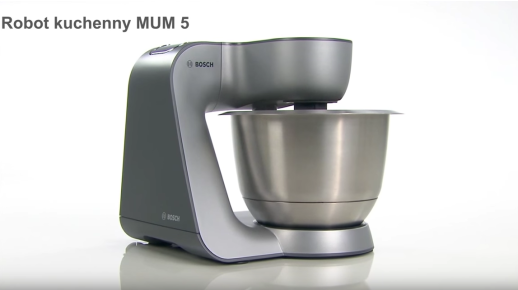 Na obrazie widoczny jest robot kuchenny w kolorze szarym z metalową misą. W lewym górnym rogu znajduje się tekst: \'Robot kuchenny MUM 5\'.