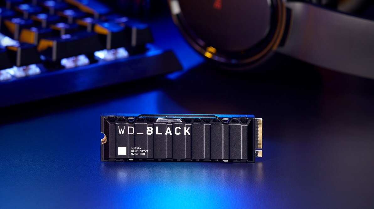 Na obrazie widoczny jest dysk SSD z napisem \'WD_BLACK\' oraz oznaczeniami \'SN850X\', \'GAME DRIVE\', \'M.2 2280\', \'NVMe SSD\'. W tle znajduje się klawiatura i słuchawki na ciemnym biurku.