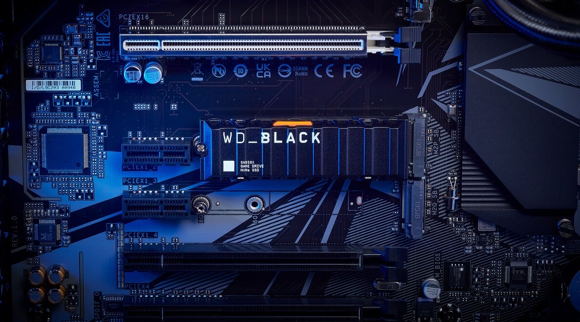 Na obrazie widoczna jest płyta główna komputera z zamontowanym dyskiem SSD oznaczonym jako WD_BLACK. W tle widać różne elementy elektroniczne i złącza PCIe.