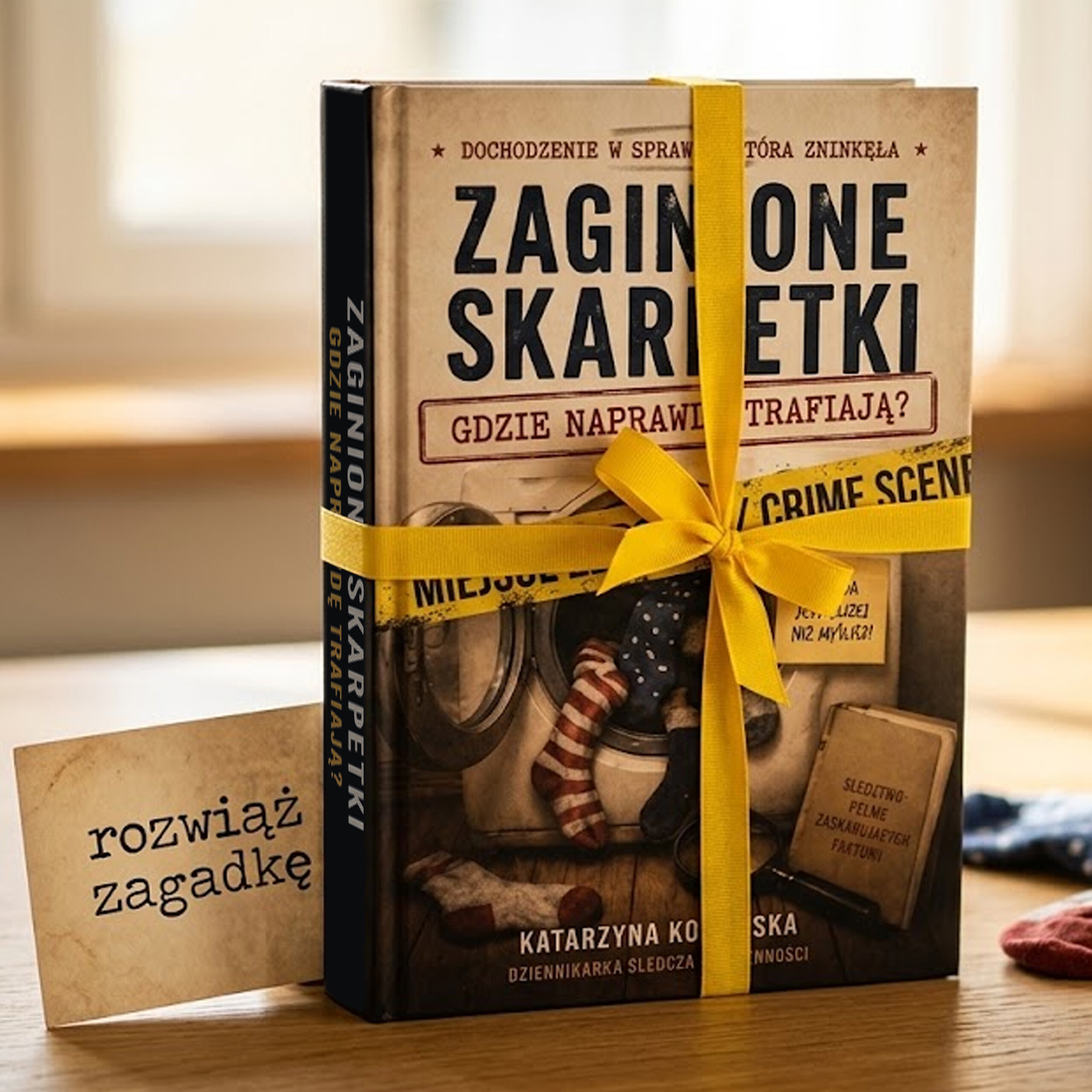 Książka zatytułowana \'Zaginione Skarpetki\' z żółtą wstążką, obok której znajduje się kartka z napisem \'rozwiąż zagadkę\'.
