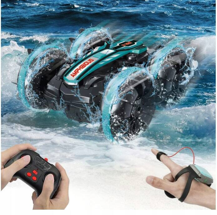 Zdalnie sterowany samochód amfibia z napisem \'Amphibious\' na masce, poruszający się po wodzie. Obok widoczne są dwie dłonie trzymające piloty do sterowania pojazdem.