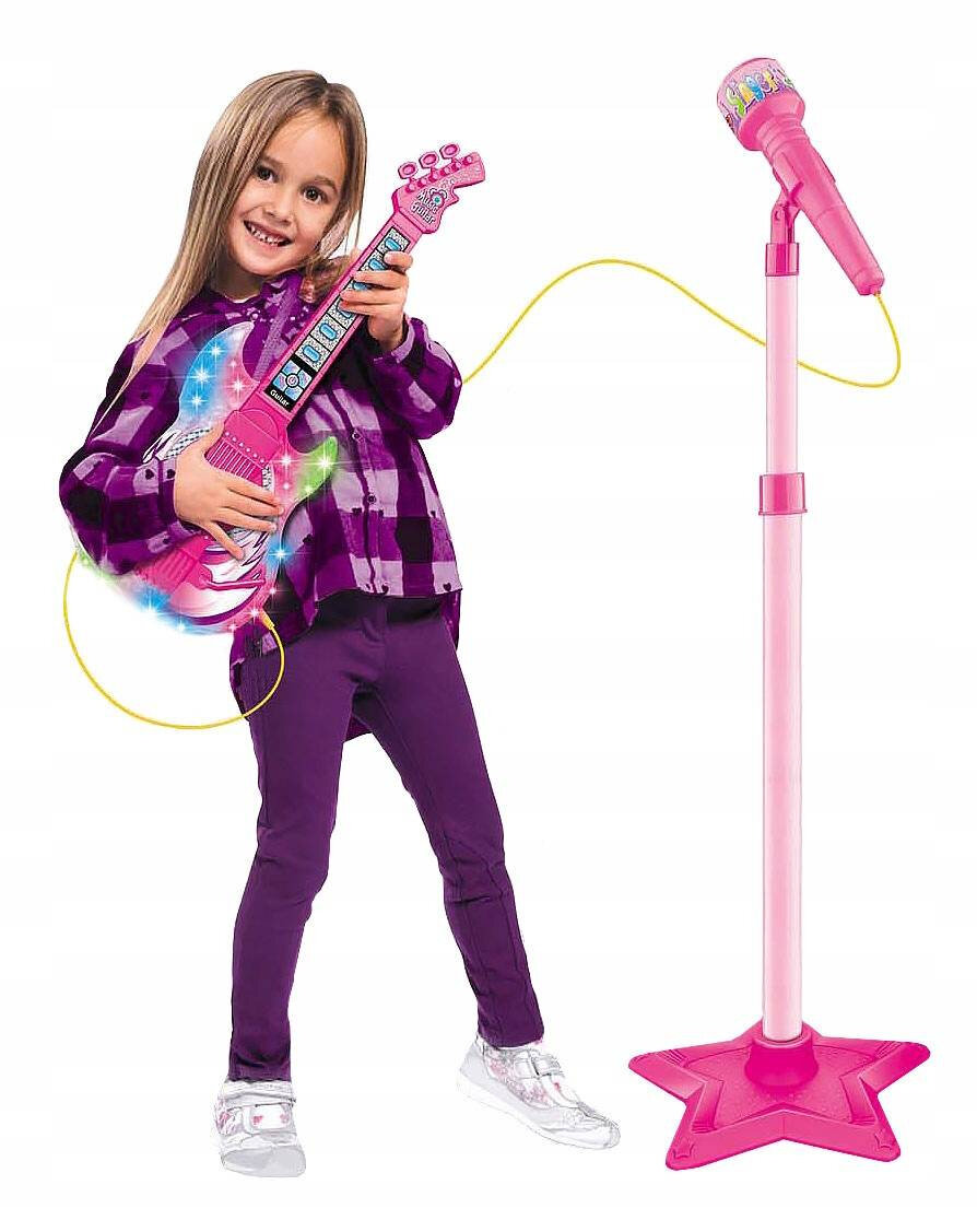 Dziecko trzyma różową gitarę elektryczną z kolorowymi światłami. Obok stoi różowy mikrofon na statywie w kształcie gwiazdy.