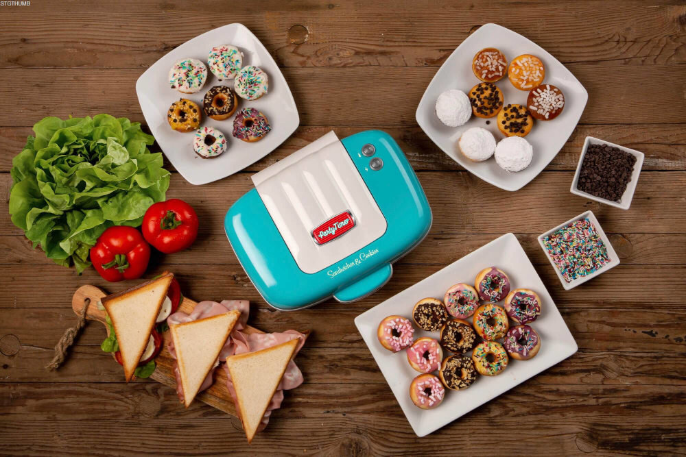 Na drewnianym stole znajduje się niebieski opiekacz z napisem \'Party Time Sandwich & Cookie\', otoczony talerzami z małymi pączkami i kanapkami, a także warzywami i posypkami.