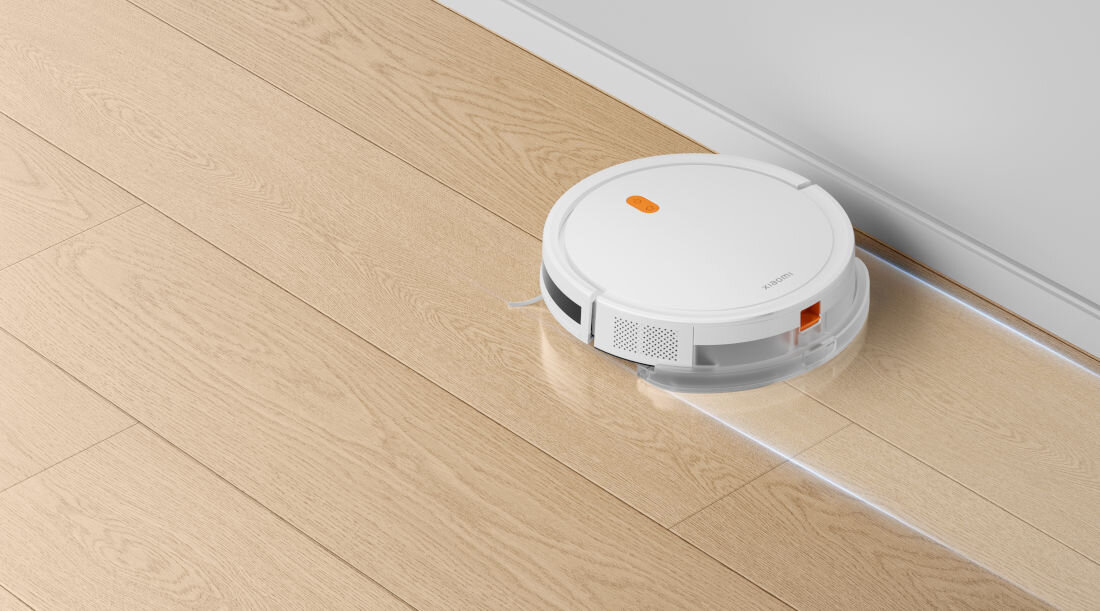 Biały robot sprzątający na drewnianej podłodze. Na urządzeniu widoczny jest napis \'XIAOMI\'.
