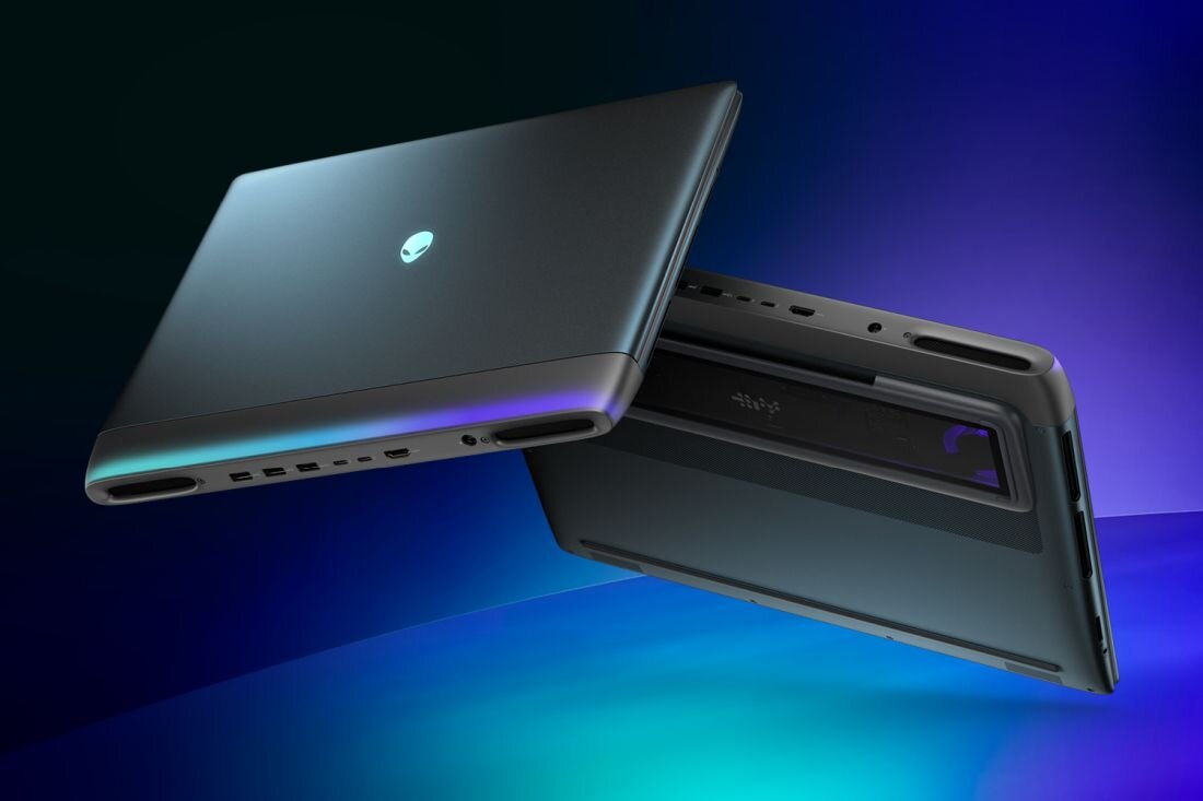 Dwa laptopy w ciemnym kolorze, jeden z widocznym logo w kształcie głowy obcego. Oba urządzenia są lekko uniesione, ukazując porty i dolną część obudowy.