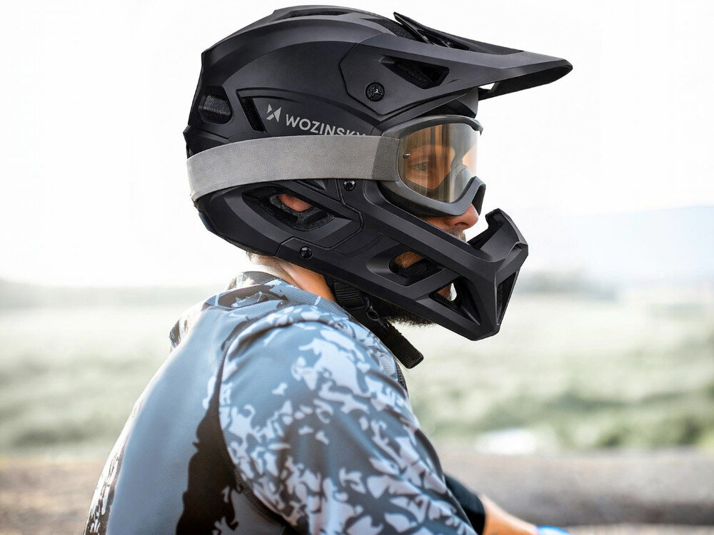 Osoba nosi czarny kask rowerowy full face marki WOZINSKY z goglami. Kask ma napis \'WOZINSKY\' i jest przeznaczony do jazdy MTB.