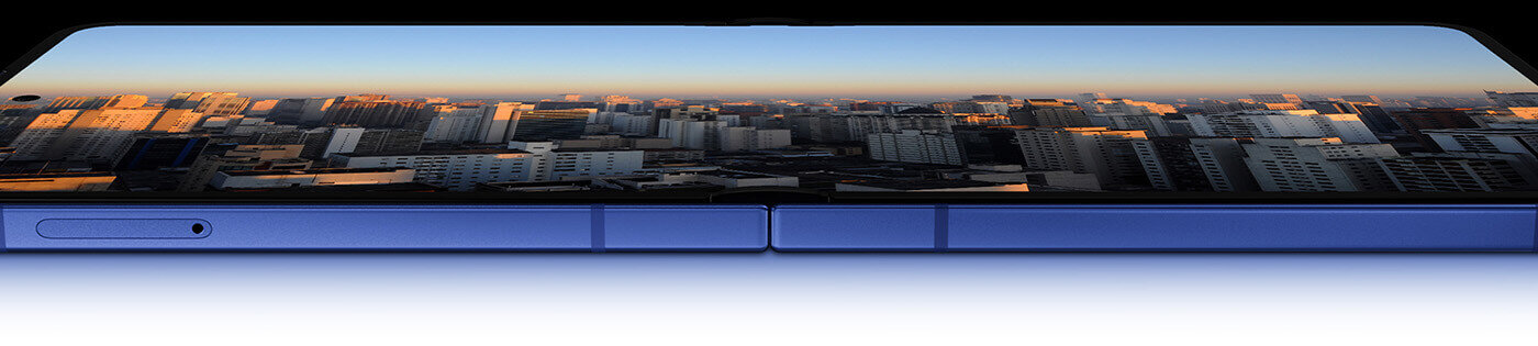 Obraz przedstawia złożony smartfon z widocznym ekranem, na którym wyświetla się panorama miasta o zachodzie słońca. Obudowa urządzenia jest w kolorze niebieskim.