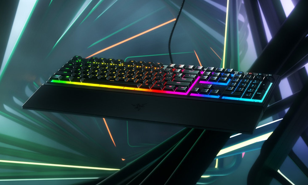 Klawiatura z podświetleniem RGB w różnych kolorach, z widocznym logo producenta na środku. W tle geometryczne kształty i linie świetlne.