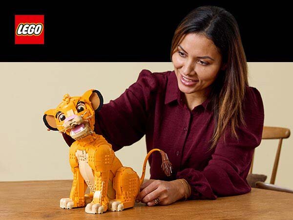 Na stole znajduje się model LEGO przedstawiający młodego Simbę z filmu Król Lew. W tle widoczne jest logo LEGO.