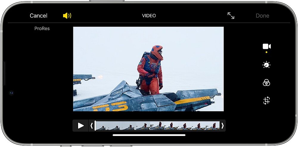 Ekran smartfona z aplikacją do edycji wideo, na którym widać kadr z filmu przedstawiający osobę w czerwonym kombinezonie stojącą na pojeździe. Na ekranie widoczne są przyciski do edycji wideo oraz pasek z miniaturami klipów.
