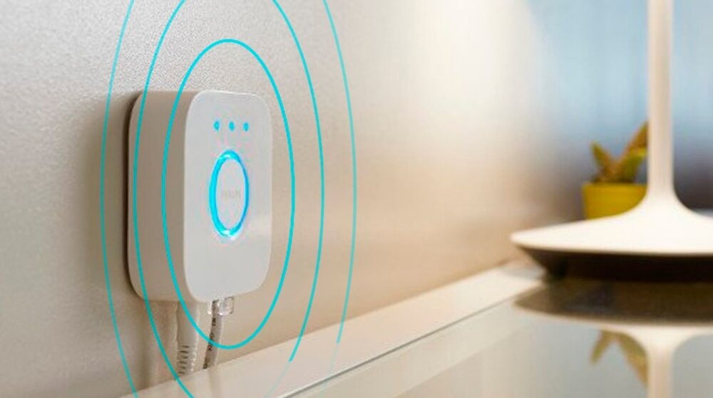 Na ścianie zamontowane jest białe urządzenie z niebieskim podświetleniem i logo \'PHILIPS\'. Obok znajduje się lampa z białym kloszem.