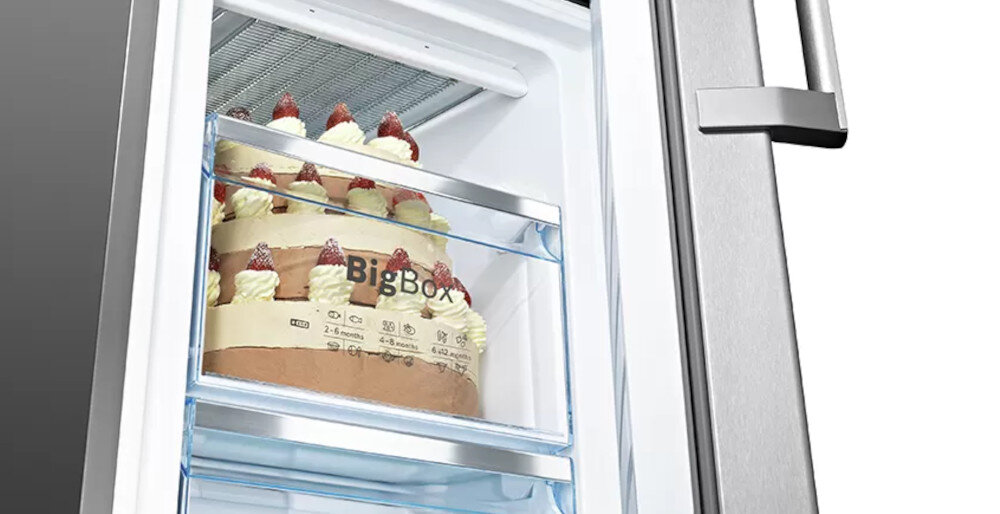 Wnętrze lodówki z widocznym dużym tortem w zamrażarce, na szufladzie napis \'BigBox\'.