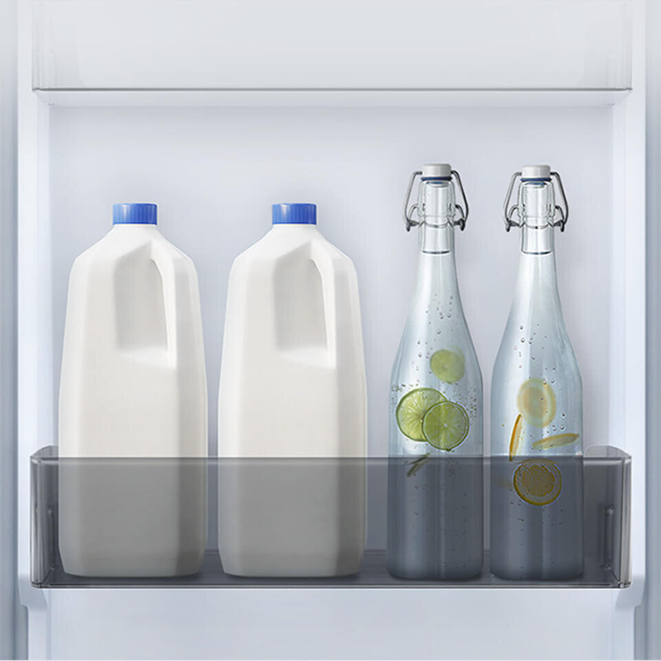 Wnętrze lodówki z dwoma plastikowymi butelkami z niebieskimi zakrętkami oraz dwiema szklanymi butelkami z plasterkami cytryny i limonki. Butelki stoją na półce drzwiowej lodówki.