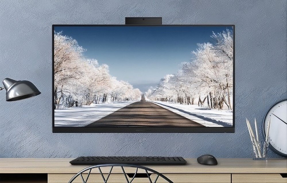 Komputer All in One ASUS V440VAT-BPD036W Czarny komputer zamontowany na niebieskiej ścianie nad drewnianym biurkiem, wyświetlający zimowy krajobraz z ośnieżoną drogą, z widoczną na blacie czarną klawiaturą oraz myszką, konstrukcja, zarządzanie kablami, zgodność z VESA