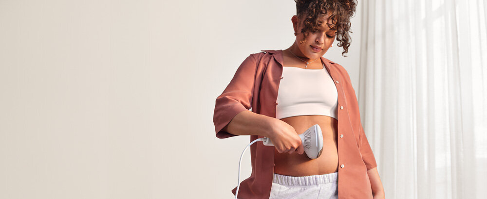Kobieta depilująca włosy na brzuchu depilatorem Philips Lumea.