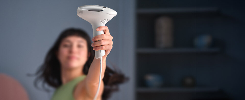 Kobieta z wyciągniętą ręką, w której trzyma depilator Philips Lumea.