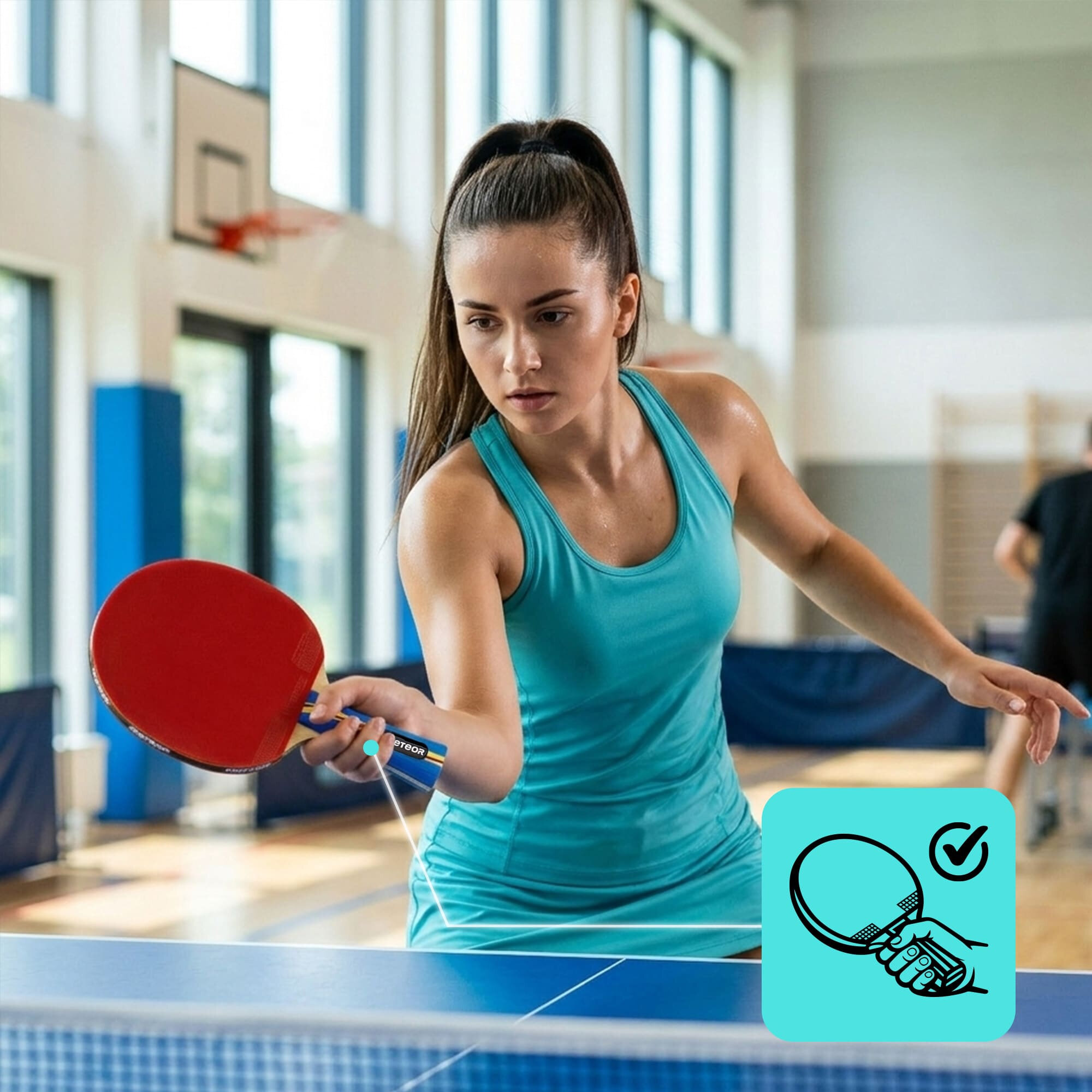 Osoba w niebieskim stroju sportowym gra w tenisa stołowego, trzymając czerwoną rakietkę. W tle widać salę gimnastyczną z oknami i koszem do koszykówki.
