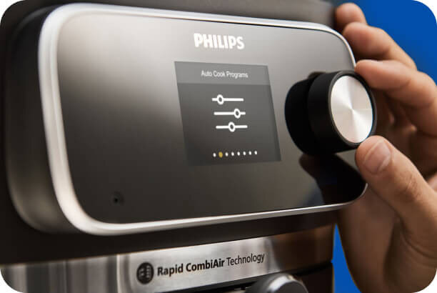 Zbliżenie na panel sterowania frytkownicy z logo PHILIPS, wyświetlaczem pokazującym \'Auto Cook Programs\' i pokrętłem. Na dole widoczny napis \'Rapid CombiAir Technology\'.