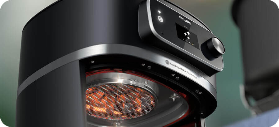 Zbliżenie na czarną frytkownicę beztłuszczową z widocznym panelem sterowania i logo \'Philips\'. Wewnątrz urządzenia widać metalowy ruszt i element grzewczy.