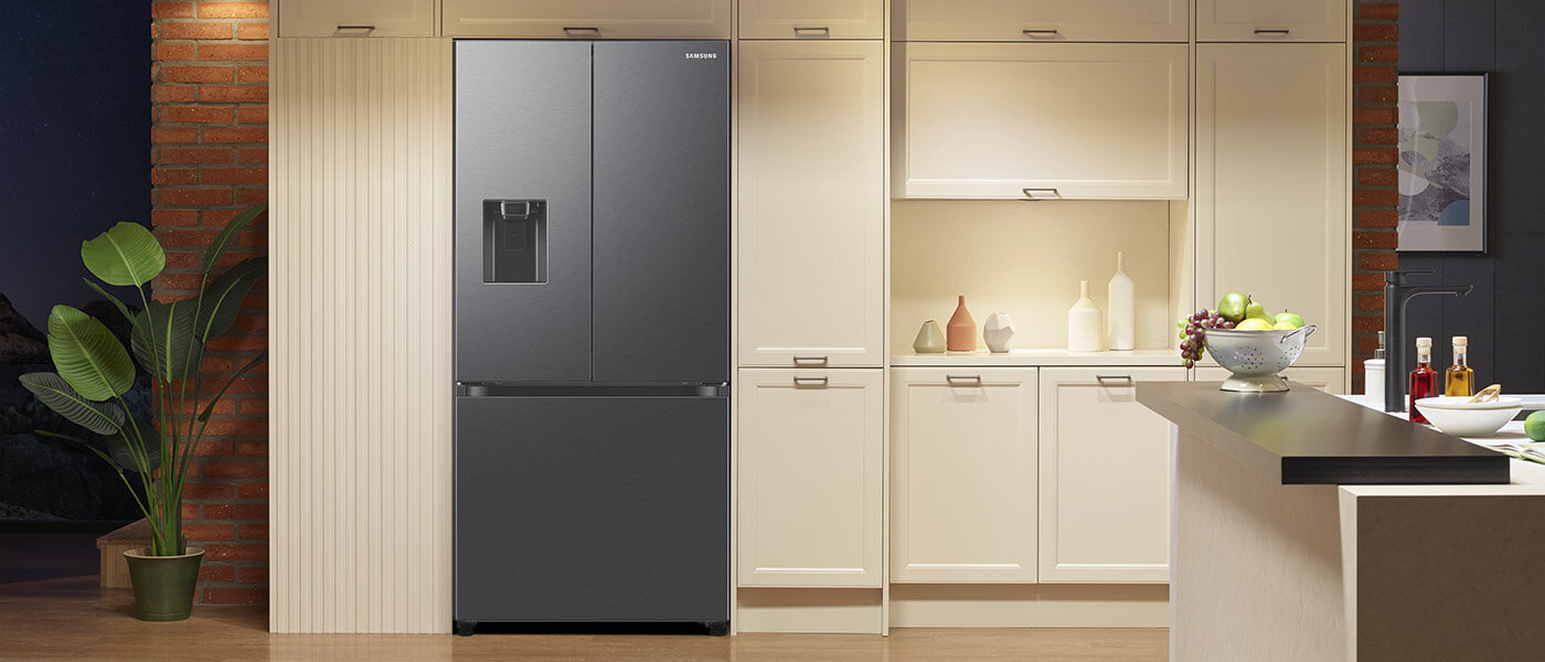Lodówka Samsung Multidoor to nie tylko funkcjonalność, ale także wyrafinowany design, który doskonale komponuje się z nowoczesnym wnętrzem kuchni Grafitowa lodówka z dwoma drzwiami i wbudowanym dystrybutorem wody stoi w nowoczesnej kuchni. Obok znajdują się jasne szafki kuchenne i dekoracje, takie jak rośliny i miska z owocami.
