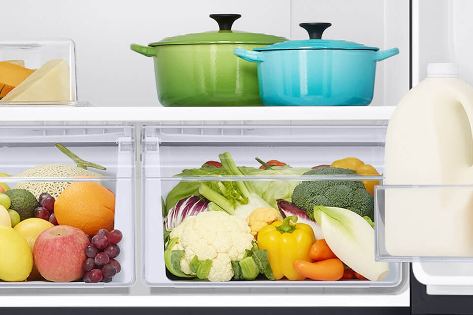Szuflady na warzywa i owoce w lodówce Samsung Multidoor to idealne miejsce do przechowywania i zachowania świeżości Twoich ulubionych produktów Wnętrze lodówki z widocznymi dwoma garnkami na górnej półce oraz różnorodnymi warzywami i owocami w dwóch dolnych szufladach. Na drzwiach lodówki znajduje się karton mleka.