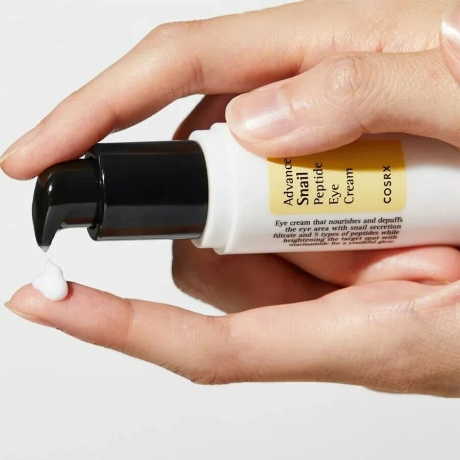 Osoba trzyma tubkę kremu z napisem \'Advanced Snail Peptide Eye Cream COSRX\', z której wyciska niewielką ilość produktu na palec. Na tubce znajduje się również tekst opisujący działanie kremu.