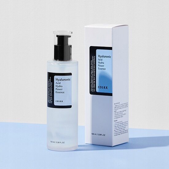 Na obrazie widoczna jest butelka z pompką oraz pudełko produktu z napisem \'Hyaluronic Acid Hydra Power Essence COSRX\'. Oba elementy mają minimalistyczny design z dominującym kolorem białym i niebieskim.