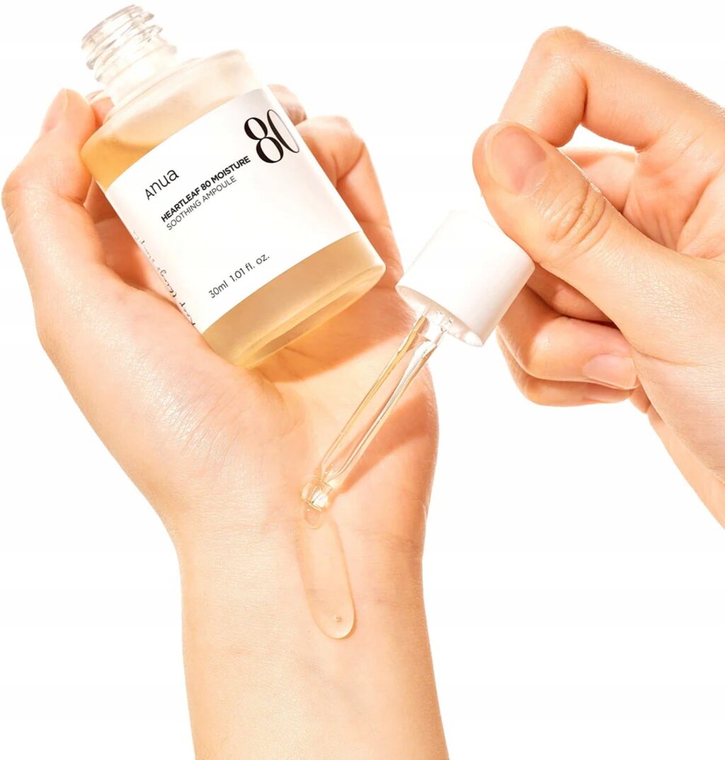 Osoba trzyma butelkę z pipetą, z której wypływa kropla płynu na skórę. Na etykiecie widoczny jest napis: \'Anua Heartleaf 80 Moisture Soothing Ampoule 30ml 1.01 fl. oz.\'.