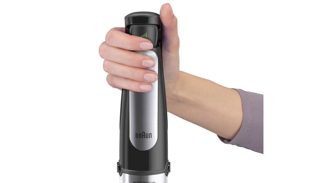 Osoba trzyma w ręku czarny blender z widocznym logo \'BRAUN\' na obudowie. Blender ma metaliczne wykończenie i ergonomiczny uchwyt.