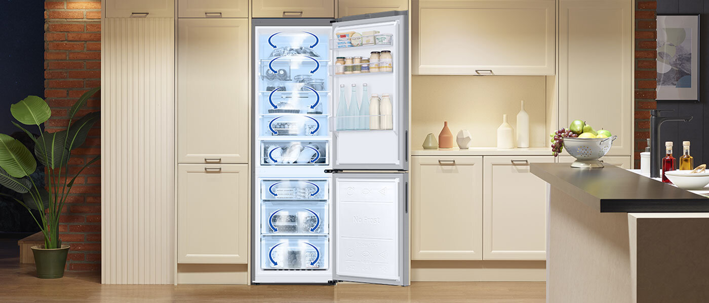 Za pomocą strzałek pokazano ruch powietrza w systemie All-Around-Cooling zastosowanym w lodówkach Samsung Kuchnia z otwartą lodówką, w której widać kilka półek z produktami spożywczymi. Wnętrze lodówki jest jasno oświetlone, a obok znajdują się szafki kuchenne i blat z owocami.