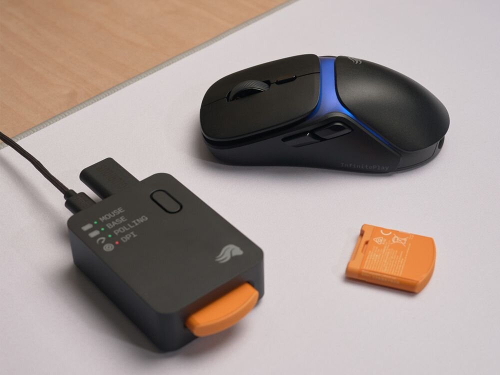Na obrazie znajduje się czarna mysz komputerowa z niebieskim podświetleniem oraz urządzenie z napisem \'MOUSE\', \'BATTERY\', \'POLLING\', \'DPI\' i logo producenta. Obok leży pomarańczowy element z oznaczeniami technicznymi.