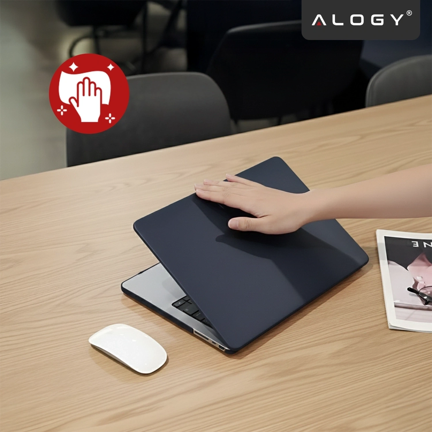 Na drewnianym stole znajduje się laptop z granatowym etui, na którym spoczywa dłoń. Obok leży biała myszka i magazyn, a w rogu widoczne jest logo \'ALOGY\'.