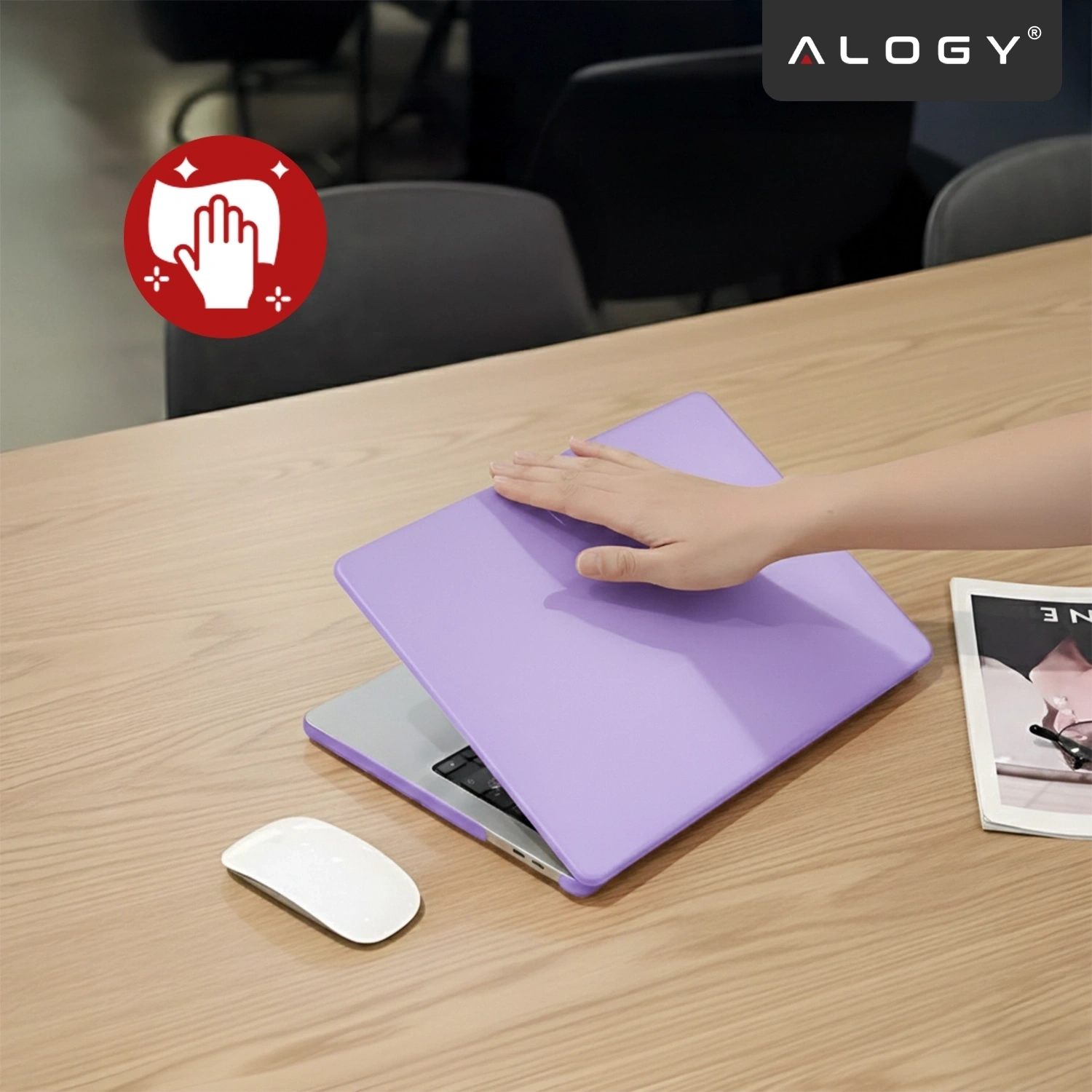 Na drewnianym stole znajduje się laptop z fioletowym etui, na którym spoczywa dłoń. Obok leży biała myszka i magazyn, a w rogu widoczne jest logo \'ALOGY\'.