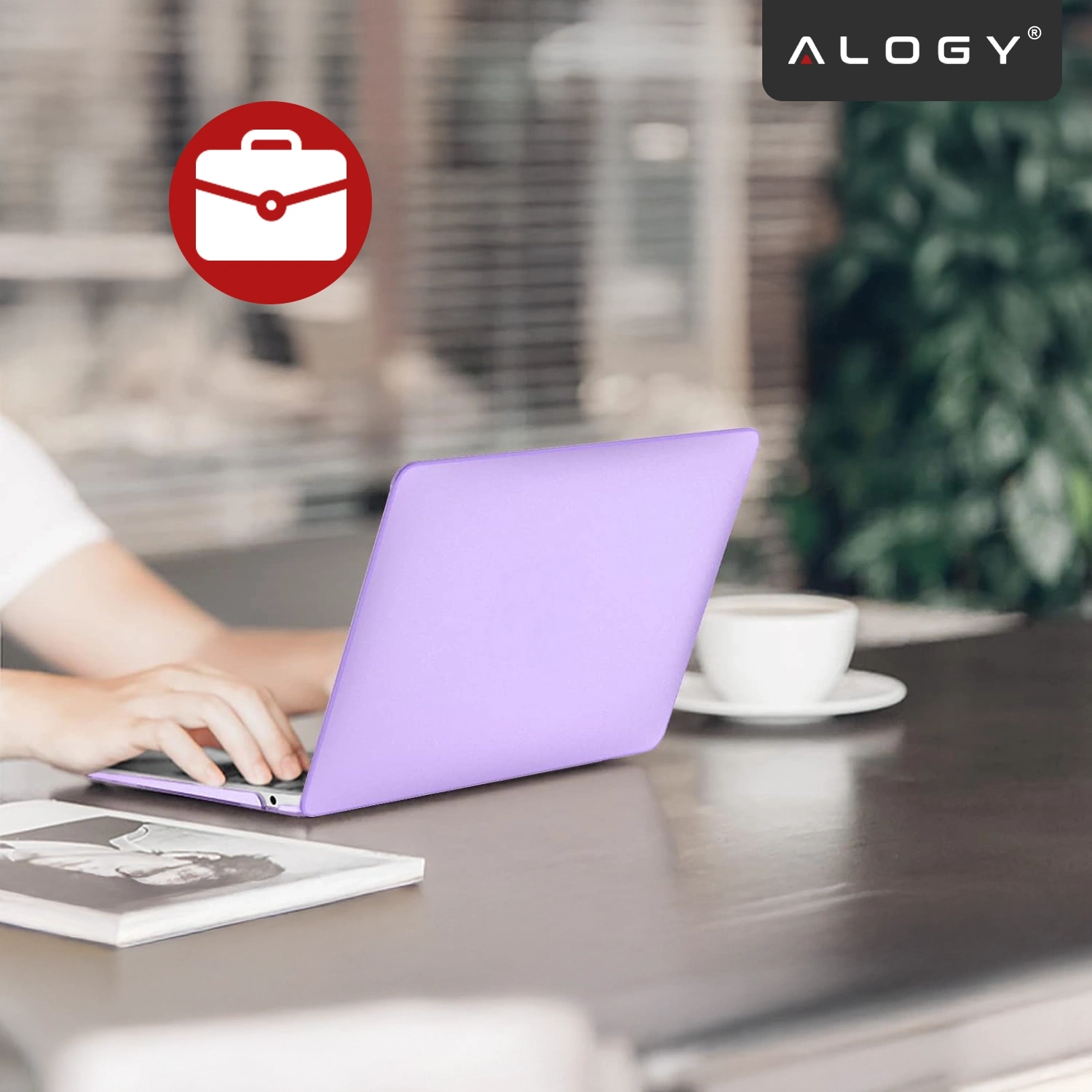 Osoba korzysta z laptopa z fioletowym etui na biurku, obok znajduje się filiżanka kawy. W prawym górnym rogu widoczne jest logo \'ALOGY\'.