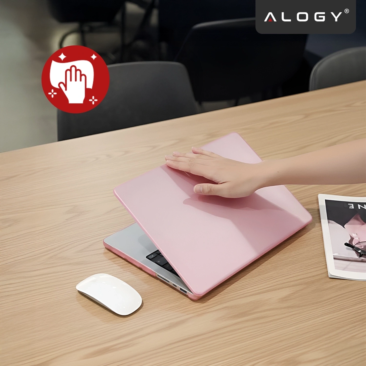 Na drewnianym stole znajduje się różowe etui na laptopa, na którym spoczywa dłoń. W tle widoczne jest logo \'ALOGY\'.