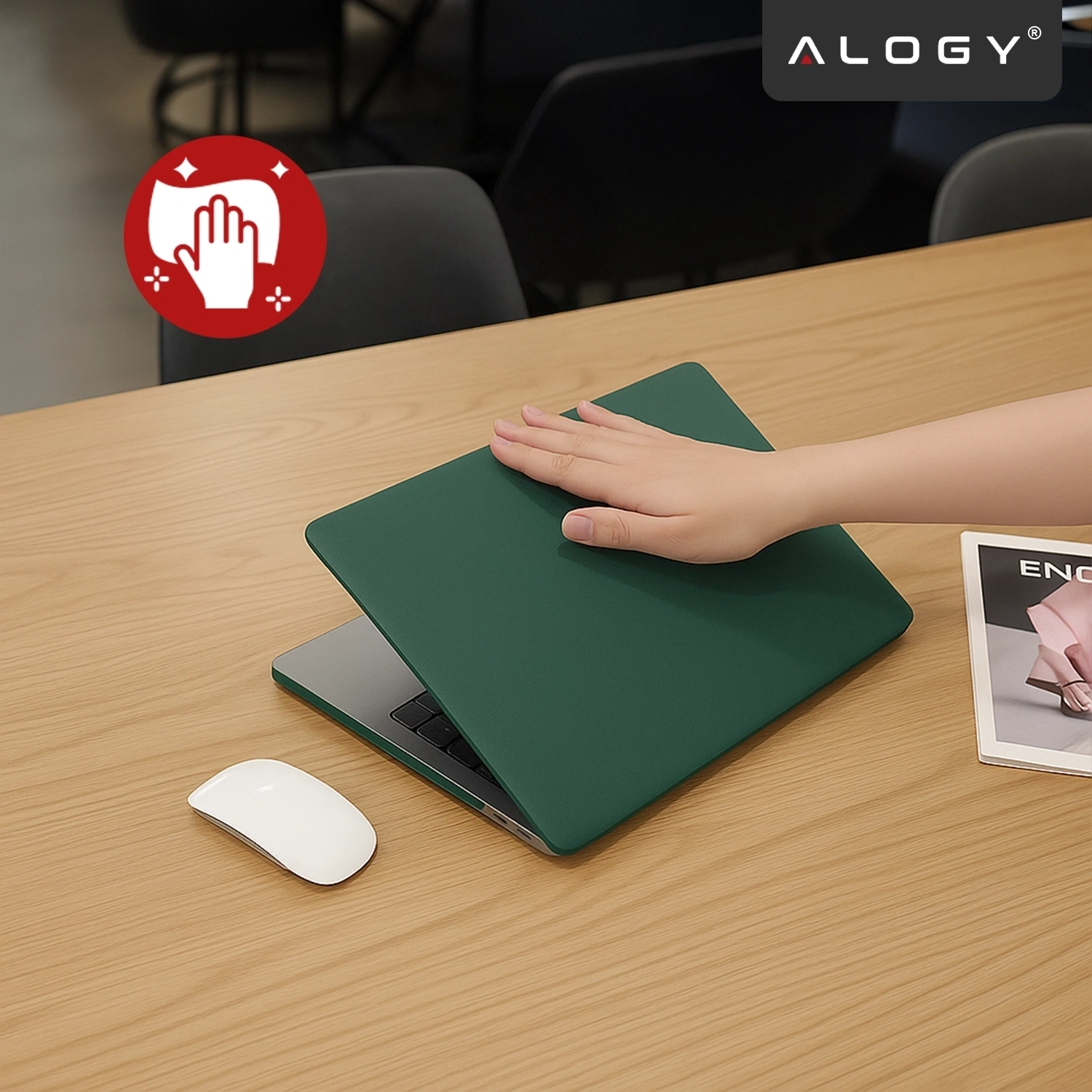 Na drewnianym stole znajduje się laptop z zielonym, matowym etui, na którym spoczywa dłoń. Obok leży biała myszka i magazyn, a w rogu widoczne jest logo \'ALOGY\'.
