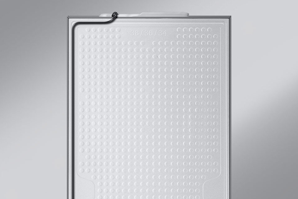 Metalowe wykończenie Clean Back dodatkowo chroni lodówkę i ogranicza hałas Widoczna jest wewnętrzna część drzwi lodówki z białą, perforowaną powierzchnią i cienką rurką wzdłuż krawędzi. Na górze widoczny jest napis \'28/36/34\'.