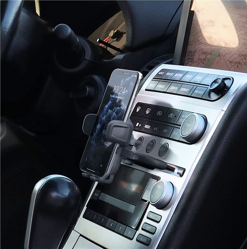 Uchwyt samochodowy zamontowany w szczelinie na płyty CD, trzymający smartfon z wyświetlonym ekranem. W tle widoczna jest konsola samochodowa z przyciskami i pokrętłami.