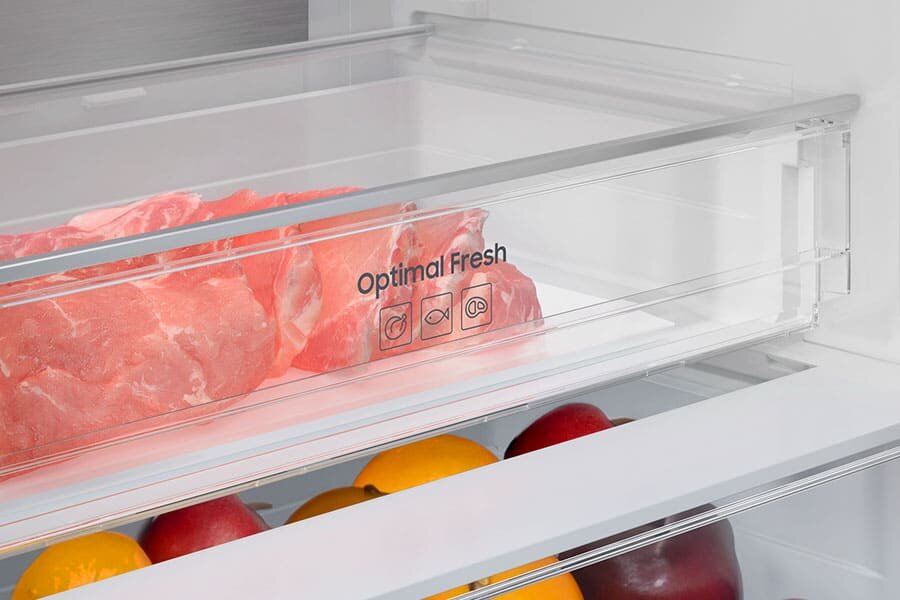 Optimal Fresh - Samsung RB53DG703DS9 - Media Expert Wnętrze lodówki z przezroczystą szufladą oznaczoną napisem \'Optimal Fresh\', w której znajduje się surowe mięso. Poniżej widoczne są owoce, w tym cytryny i jabłka.
